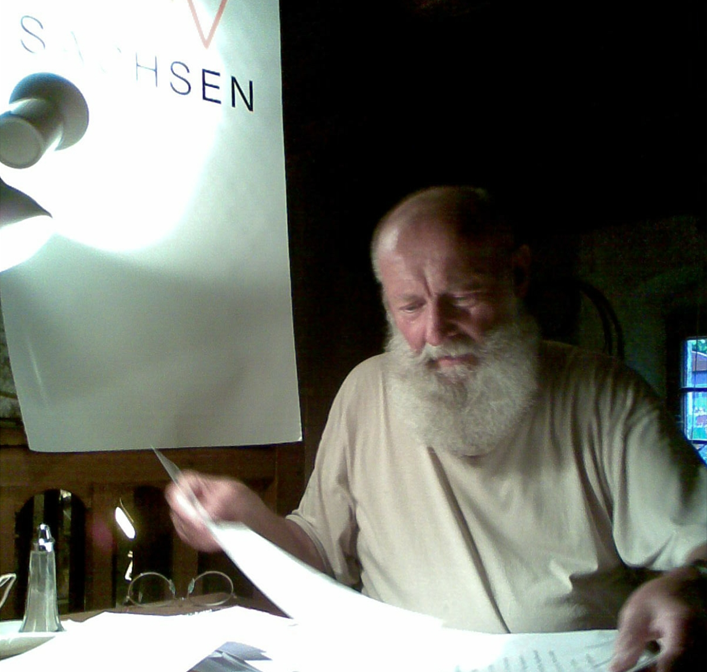 Foto Klaus Wilk sitzt am Schreibtisch und liest in einem Manuskript. – Klaus Wilk schrieb und las auch für den DJV. Foto: M.Hiller